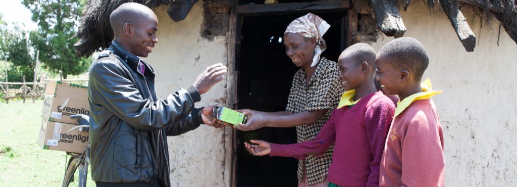 A distributor delivers solar lanterns to a mother and her two children, living at the 'last inch of the last mile' by bicycle