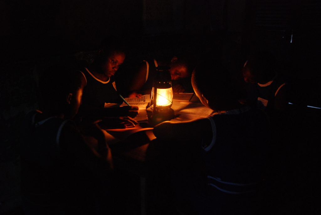 A group of children huddle around a table to study, with only the dim unhealthy light of a kerosene lamp to see.